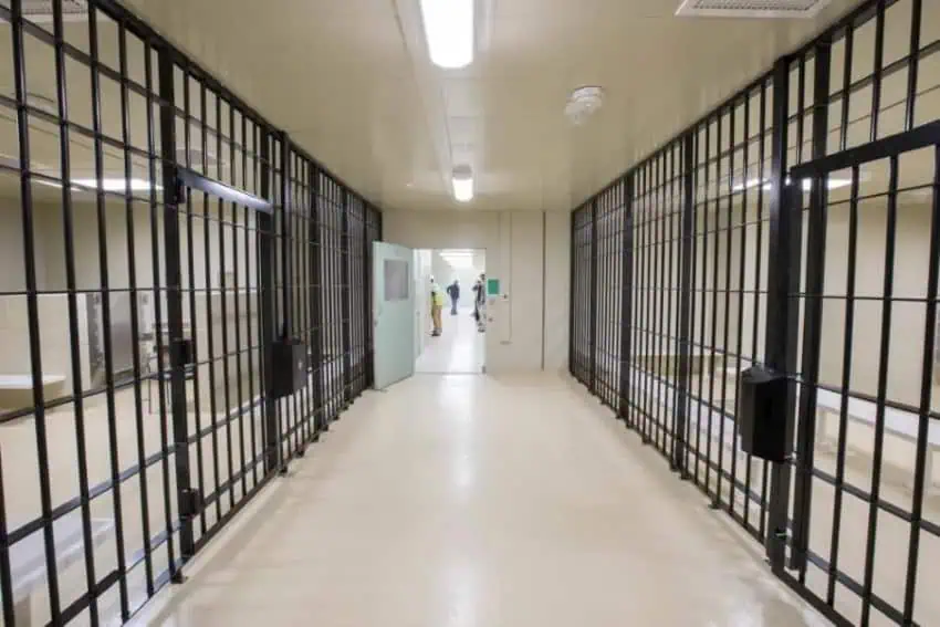 A barrier center with prisons in a hallway leads to an open door where people are found in another hall in the distance