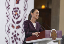 Sheinbaum smiles from behind a podium during her morning press conference