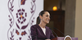 Sheinbaum smiles from behind a podium during her morning press conference