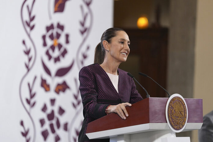 Sheinbaum smiles from behind a podium during her morning press conference