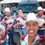 A norteño band of musicians in cowboy hats and colorful shirts take a selfie together