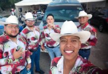 A norteño band of musicians in cowboy hats and colorful shirts take a selfie together