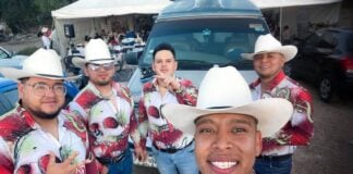 A norteño band of musicians in cowboy hats and colorful shirts take a selfie together
