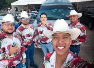 A norteño band of musicians in cowboy hats and colorful shirts take a selfie together
