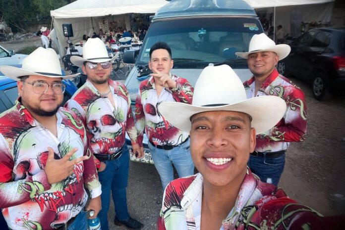 A norteño band of musicians in cowboy hats and colorful shirts take a selfie together