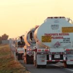 Oil tankers drive down a highway at sunset