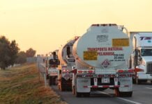 Oil tankers drive down a highway at sunset