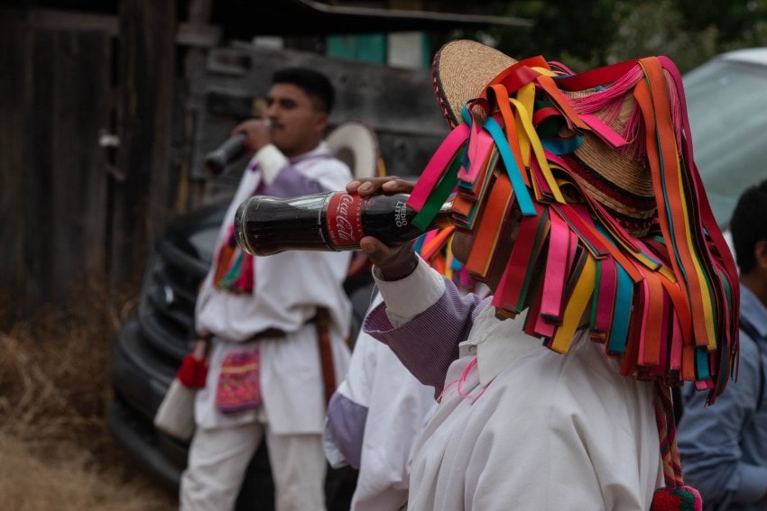 An Indigenous Tzotzil residents in traditional clothing stand in the streets of San Cristobal de las Casas, Chiapas, drinking bottles of Coca Cola.
