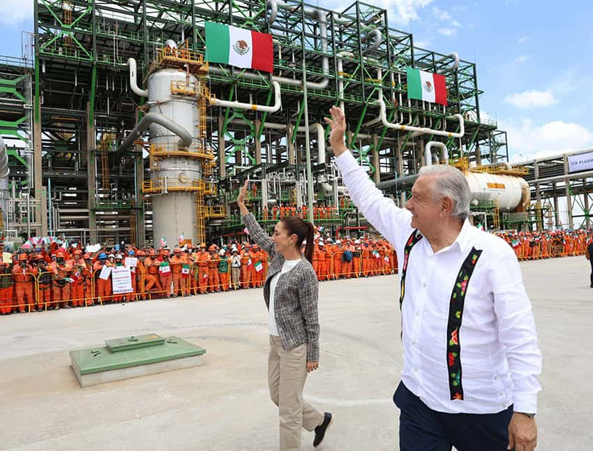 Sheinbaum and AMLO wave as they walk through a refinery
