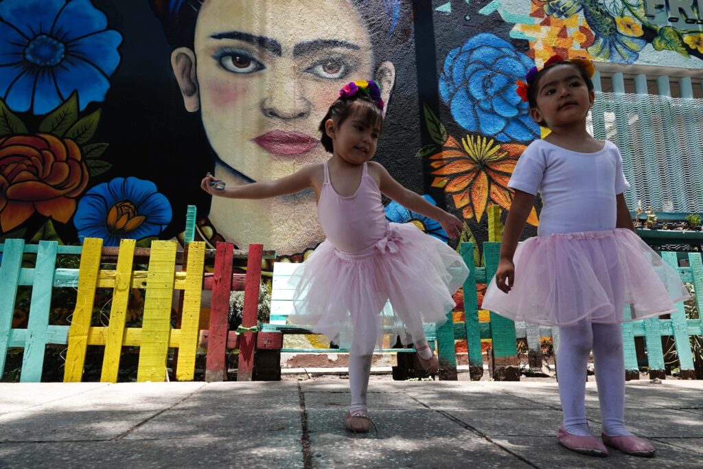 Two young girls in ballerina wear in front of a Frida Kahlo mural.