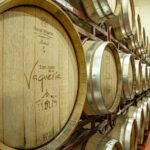 Two shelves with three rows each of wooden wine barrels with metal around their lids.