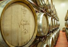 Two shelves with three rows each of wooden wine barrels with metal around their lids.