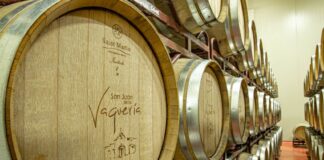 Two shelves with three rows each of wooden wine barrels with metal around their lids.