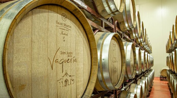 Two shelves with three rows each of wooden wine barrels with metal around their lids.