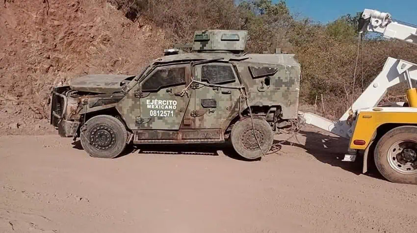 A tow truck pulls a destroyed camo Sandcat armored vehicle