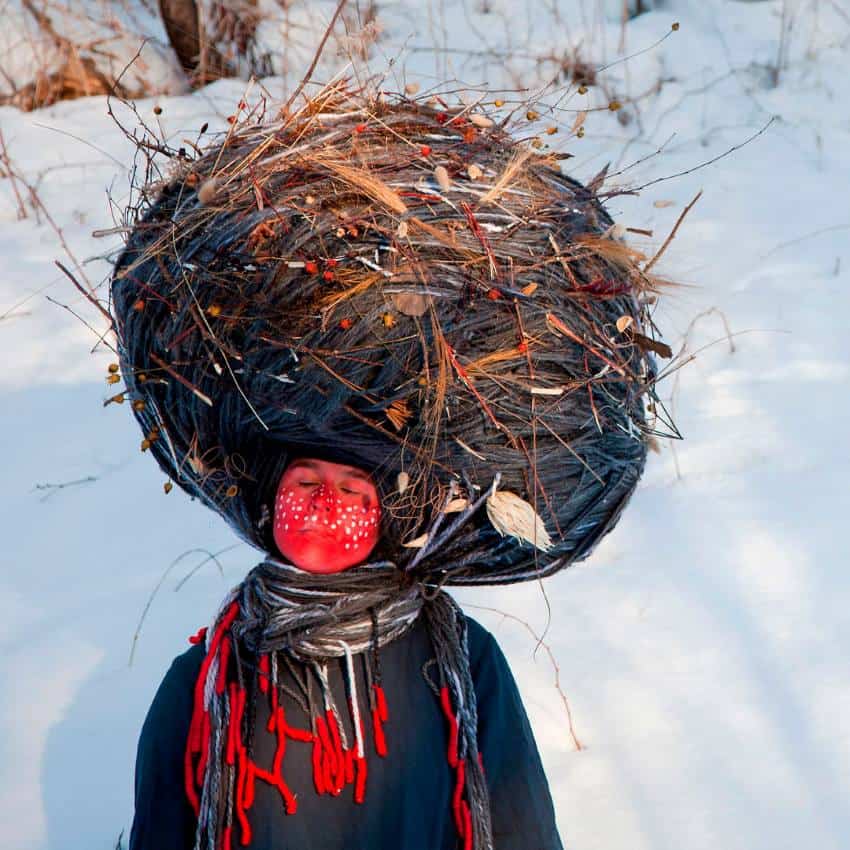 A woman's photoshop film with her face was painted red with the white spots of the paint all over her cheeks and nose. She wears yarn, straw and other natural things and a dress. His photo is exaggerated in a Woody area with a dense snow.