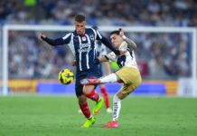 Two soccer players in Mexico in a heated bid for control of the ball during a stadium game. One man is trying to kick the ball away from the other player, who is holding him back with his hand.