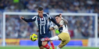 Two soccer players in Mexico in a heated bid for control of the ball during a stadium game. One man is trying to kick the ball away from the other player, who is holding him back with his hand.
