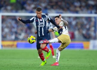 Two soccer players in Mexico in a heated bid for control of the ball during a stadium game. One man is trying to kick the ball away from the other player, who is holding him back with his hand.