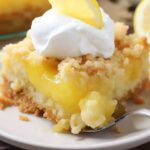 A slice of lemon cake with whipped cream and a fork