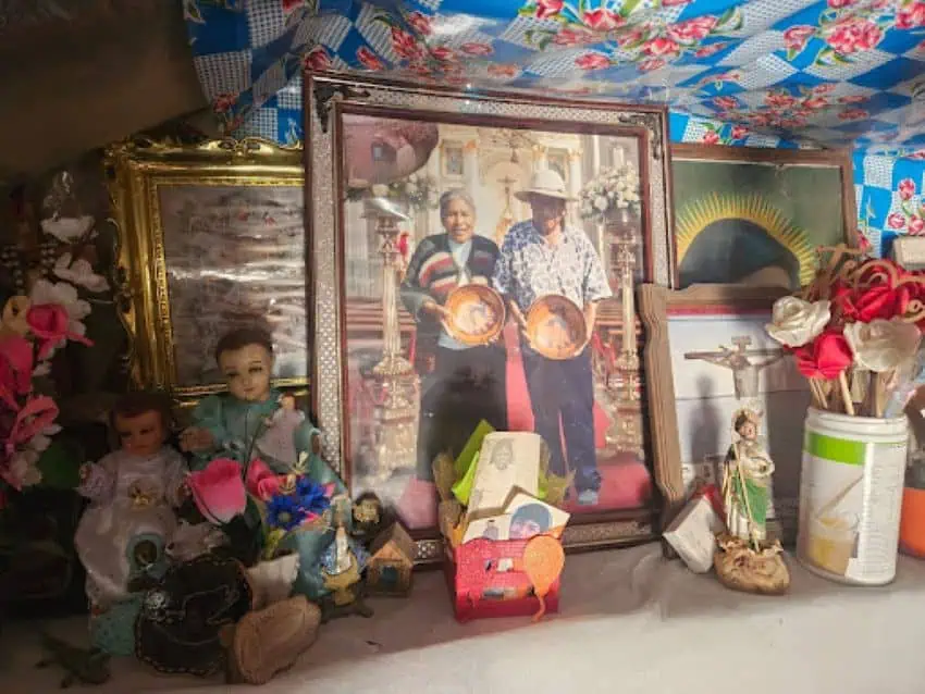 A table with some different structured photos and paintings, some Christians in nature. A photo of an elderly man and woman in the center of the craftsman holding pottery bowls in front of them.