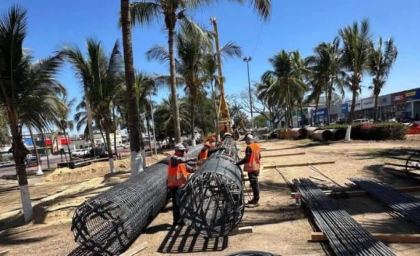 Construction workers unrolling large tubes of cable in a long dirt area surrounded by palm trees in Puerto Vallarta