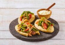 Three tlacoyos topped with peppers and onions, sitting on a serving platter made of volcanic rock. Also on this platter is a small wooden bowl of white rice with a matching wooden spoon for serving.