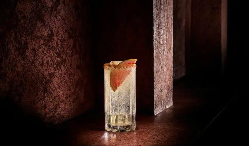 Clear cocktail in a glass beer mug sitting on a darkly stained wooden surface.