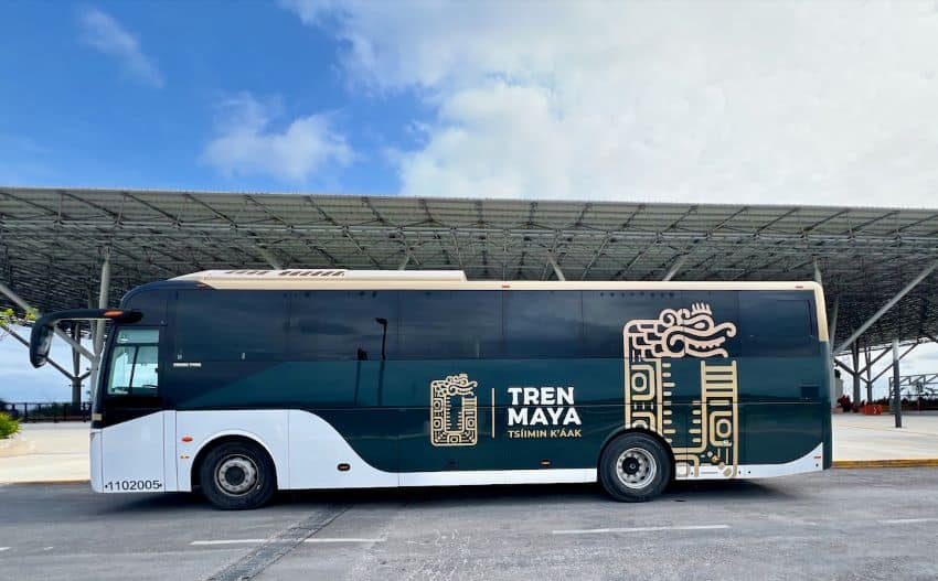 Passenger bus with Maya Train livery in front of a train station, daytime