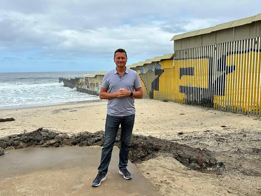 Travis Stands in front of the border wall in the Pembenke Tijuana, where it meets the sea
