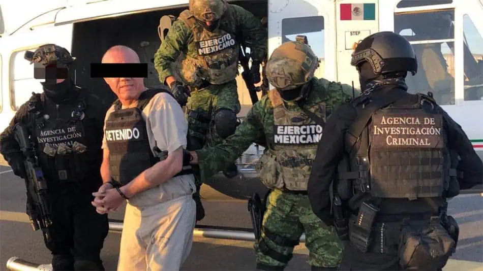 AIC agents and soldiers transport a prisoner in a bullet proof vest.