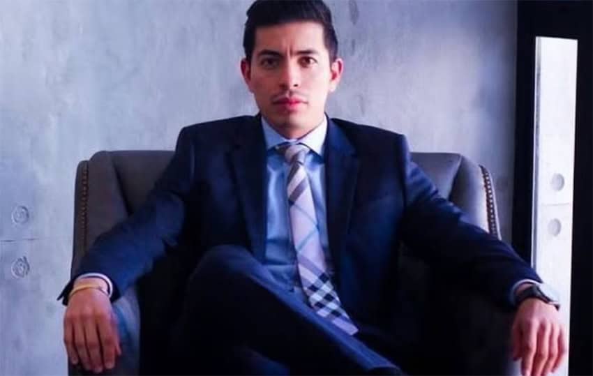 A Latino man in a business suit sits in a chair