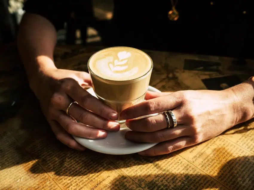 The hands of the person holding a coffee in a mirror set in a white meal on a table