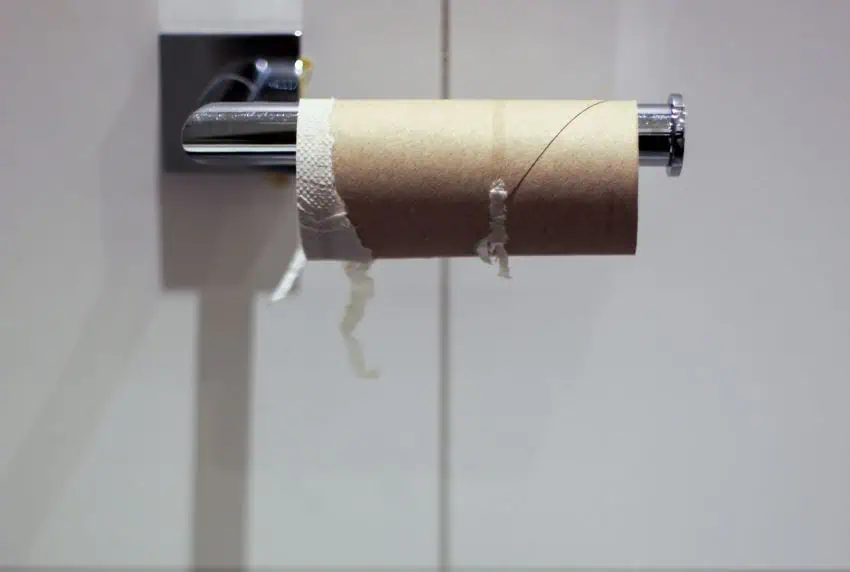A empty toilet paper roll hanging on a holder screwed to a white wall