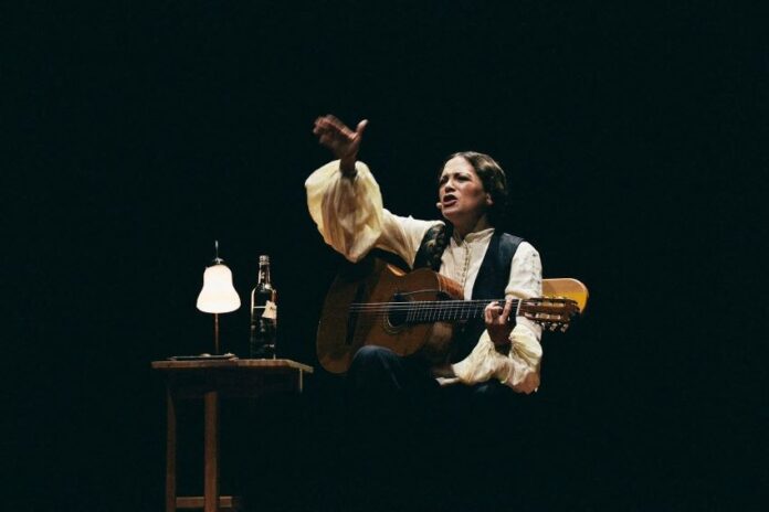Natalia Lafourcade seated onstage with guitar during Cancionera tour