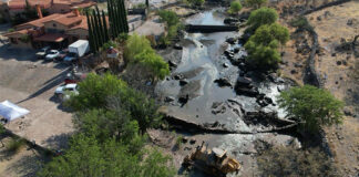 Heavy machinery sits in a river bed with a partly demolished dam, next to a large hacienda-style house