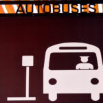 A sign in Puerto Vallarta indicating a bus hub with a icon of a man driving a bus pulling up to a bus stop sign and the word "Autobuses" on top of the sign.