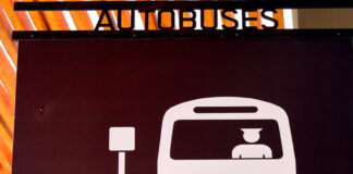 A sign in Puerto Vallarta indicating a bus hub with a icon of a man driving a bus pulling up to a bus stop sign and the word "Autobuses" on top of the sign.