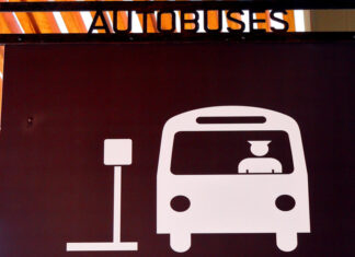 A sign in Puerto Vallarta indicating a bus hub with a icon of a man driving a bus pulling up to a bus stop sign and the word "Autobuses" on top of the sign.