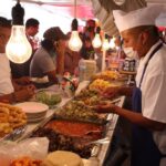 Mexico City residents standing and sitting at a temporary taco stand while waiting for employees to fill their tacos with cooked items in buffet trays.