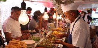 Mexico City residents standing and sitting at a temporary taco stand while waiting for employees to fill their tacos with cooked items in buffet trays.