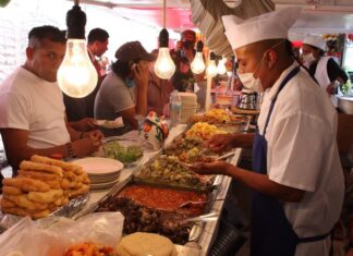 Mexico City residents standing and sitting at a temporary taco stand while waiting for employees to fill their tacos with cooked items in buffet trays.