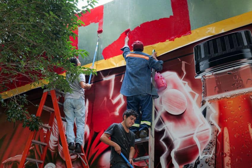 Workers with paint rollers creating an ad for Coca-Cola in a Mexico City neighborhood.