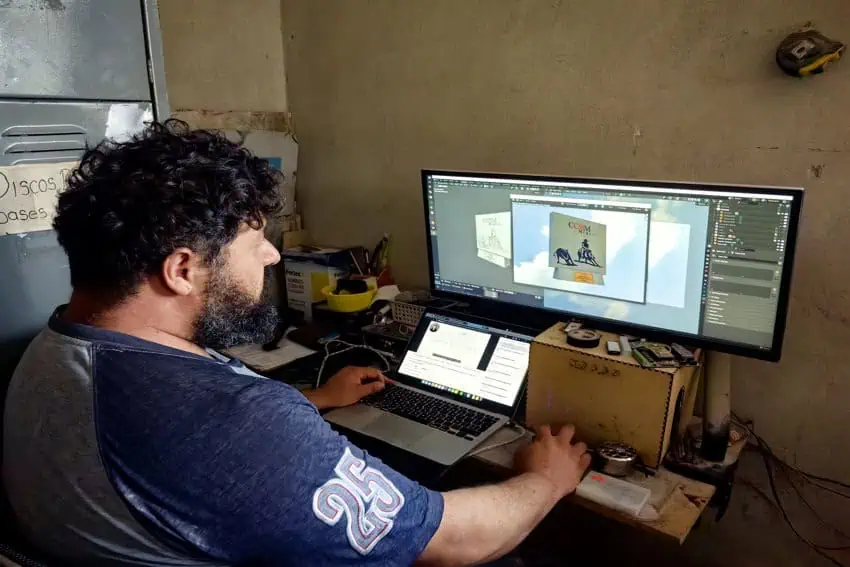 Hugo Uribe's brother, José, working on a large computer screen with a small laptop inside their family workshop office.