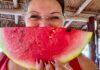 Woman posing in a Mexican palapa structure with a wedge of ripe watermelon in front of her face.