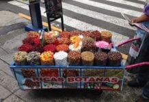 Cart of candies on a city street. Cart reads "Botanas"