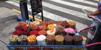 Cart of candies on a city street. Cart reads "Botanas"