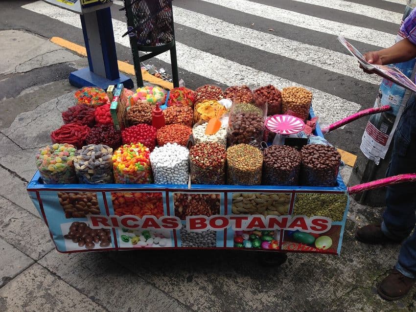 Cart of candies on a city street. Cart reads "Botanas"