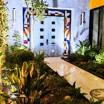 A modern Mexican courtyard with parquet floor and stone double entrance doors to a home. The three sides around the doors feature modernist abstract colors of stained glass.