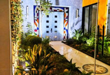 A modern Mexican courtyard with parquet floor and stone double entrance doors to a home. The three sides around the doors feature modernist abstract colors of stained glass.